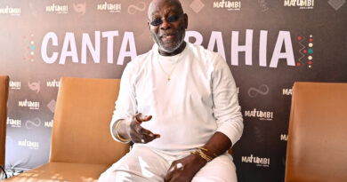 Foto do cantor Lazzo Matumbi sorrindo, sentado de roupa branca.